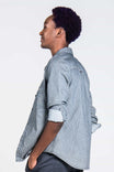 Side view of a woman wearing the Givens Work Shirt in Indigo Stripe by Dovetail Workwear, featuring visible chest pocket, cuff tabs, and lightweight striped fabric