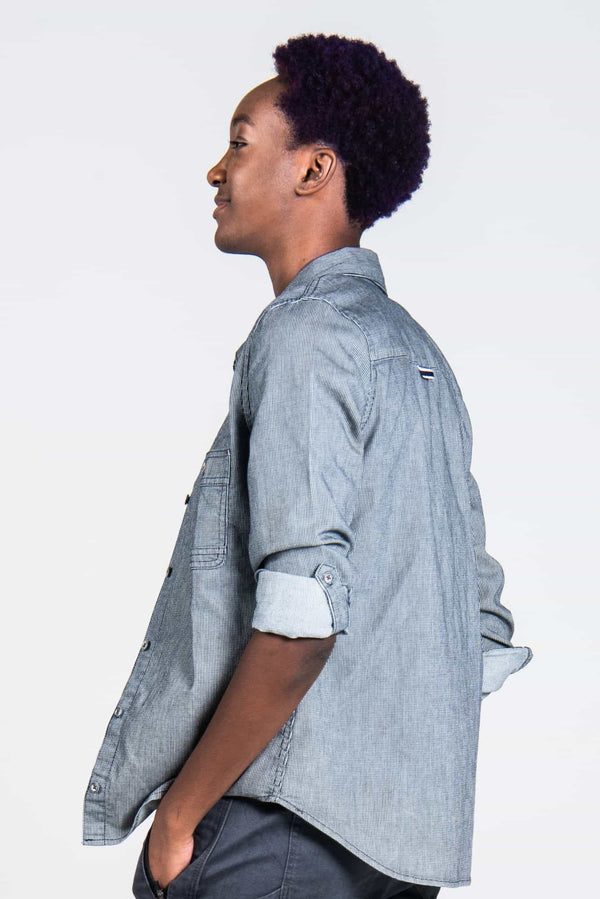 Side view of a woman wearing the Givens Work Shirt in Indigo Stripe by Dovetail Workwear, featuring visible chest pocket, cuff tabs, and lightweight striped fabric
