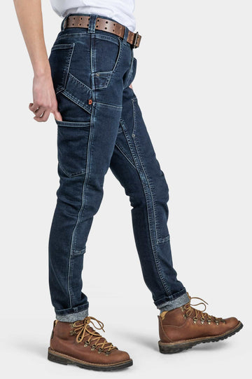 Side view of a woman wearing Dovetail Workwear Maven X in Indigo Stretch Thermal Denim with cuffed hems and brown lace-up boots