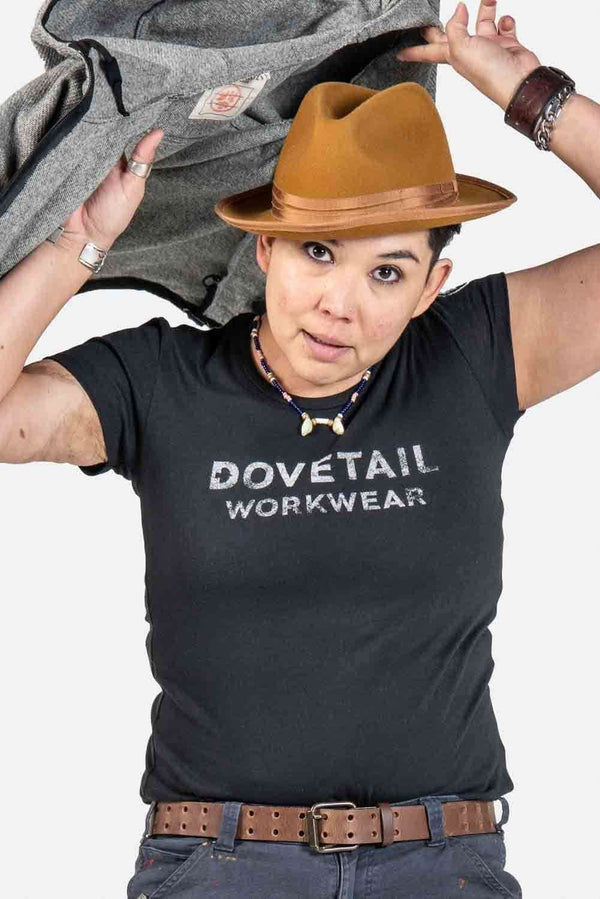 Dovetail Logo Tee worn by a woman styled with a tan cowboy hat, layered gray jacket, and brown leather belt