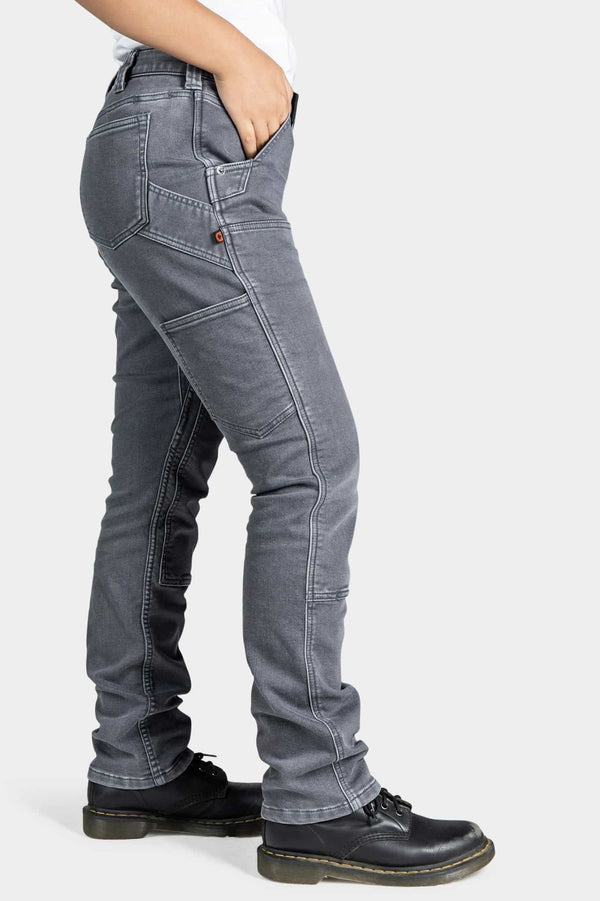 Side view of a woman wearing Dovetail Workwear's Maven X Slim Pant in Grey Stretch Thermal Denim, showing the slim leg fit, reinforced knee panel, and tool loop detail