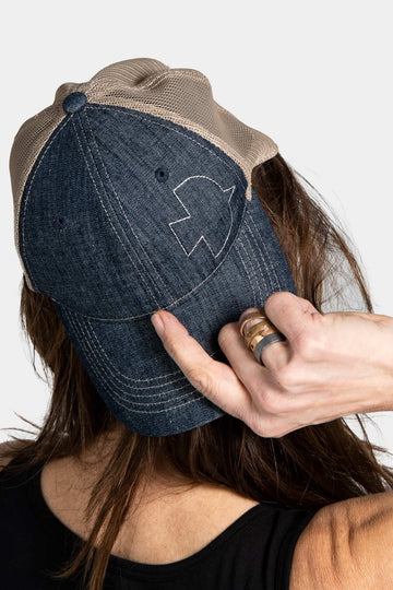 Woman holding the Dovetail Embroidered Shop Cap in blue denim with khaki mesh back, displaying the embroidered Dovetail logo on the front panel