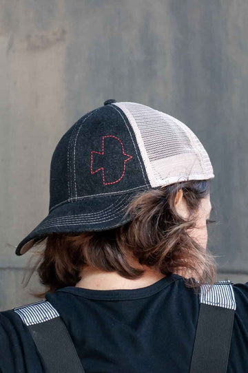 Back view of a woman wearing the Dovetail Embroidered Shop Cap in blue/black denim with white mesh panels and embroidered logo detail