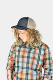 Woman wearing the Dovetail Embroidered Shop Cap in Blue/Black denim with contrasting cream mesh panels, paired with a colorful plaid shirt