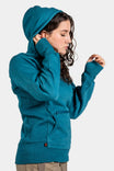 Side view of a woman wearing the Anna Pullover Hoodie in Dovetail Blue by Dovetail Workwear, featuring a hood, thumbhole cuffs, and front pockets
