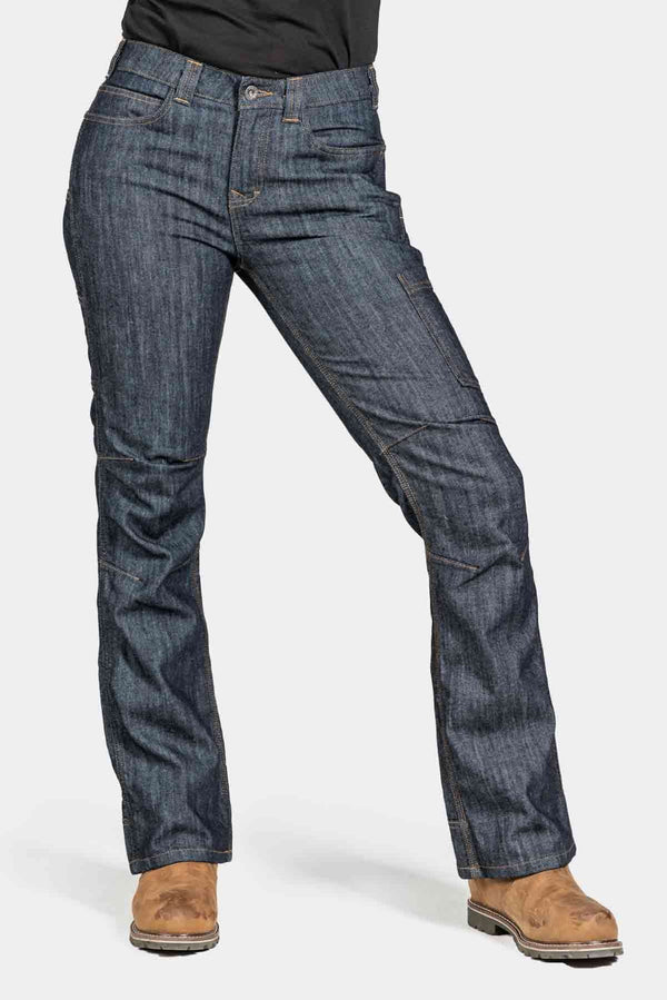 Woman wearing Dovetail Workwear DX Bootcut Pant in FR Denim indigo, shown from the side with tan boots, displaying the bootcut fit and articulated knee design