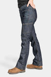 Side view of a woman wearing Dovetail Workwear's DX Bootcut Pant in FR Denim with brown boots, showing the bootcut silhouette and articulated knee design