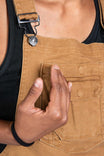 Detail view of a woman's hand touching the nested pocket on Dovetail Workwear's Freshley Overalls in Saddle Brown Canvas, showcasing the functional pocket design