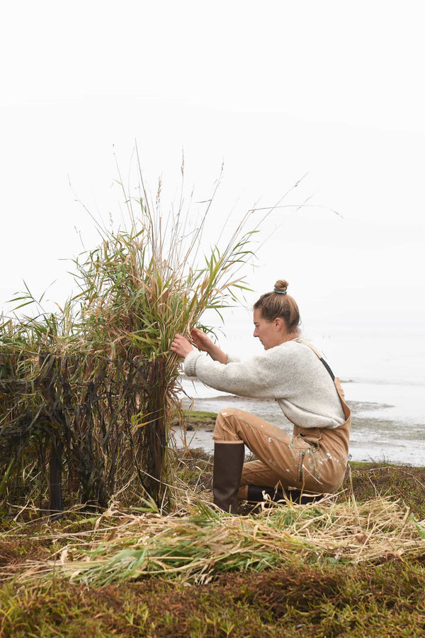 Woman crouching while gardening wearing Dovetail Workwear Freshley Overalls in Saddle Brown Canvas with reinforced knees and multiple pockets