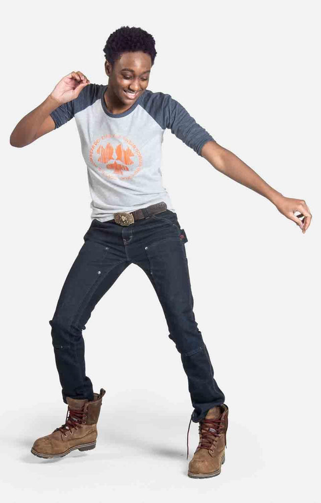 Woman modeling the Dovetail Workwear 3/4 Logo Work Shirt in charcoal with charcoal raglan sleeves, dark jeans, and brown boots in a dynamic pose