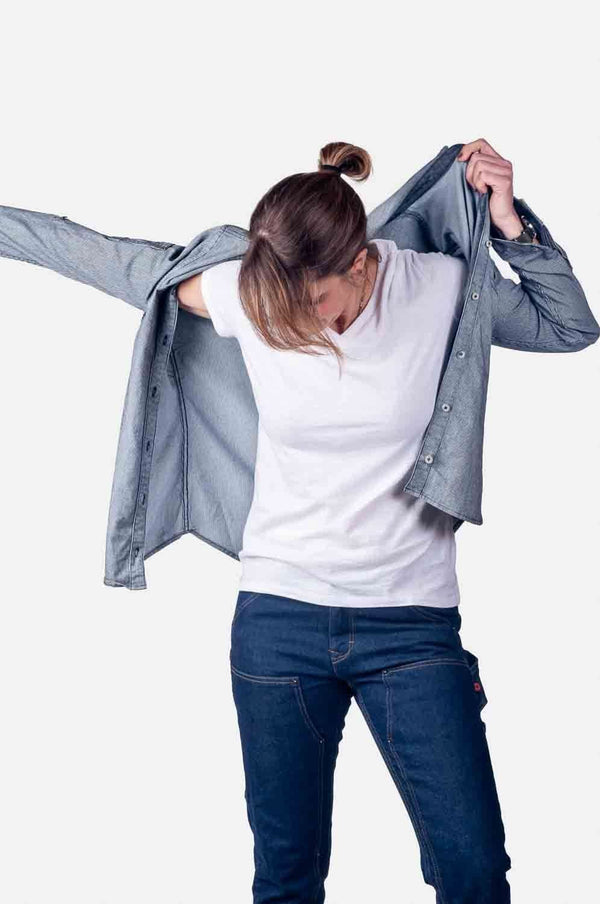 Woman wearing Dovetail Workwear's Givens Work Shirt in Indigo Stripe with arms raised, displaying the lightweight button-front design, functional chest pocket, and sleeve pocket.
