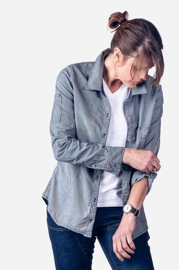 Dovetail Workwear's Givens Work Shirt in Indigo Stripe worn by a woman layered over a white tee, featuring visible chest pocket and cuff tabs