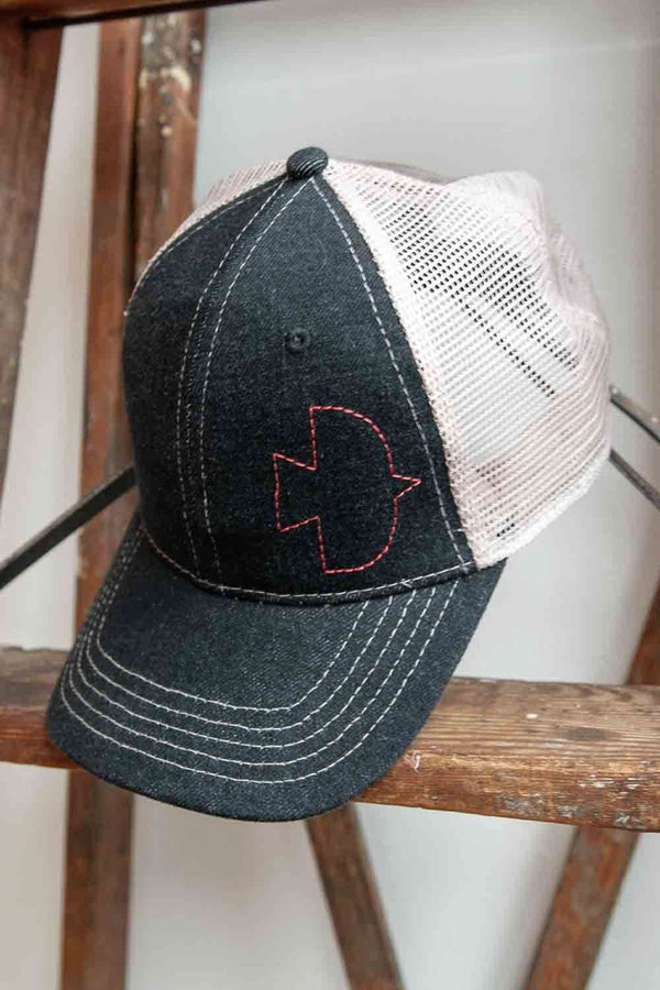 Dovetail Embroidered Shop Cap in blue denim and cream mesh, displayed on a wooden stand showing the contrasting embroidered Dovetail logo on the front
