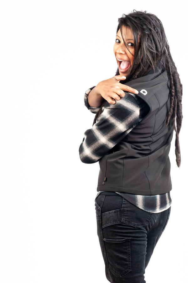 Woman wearing the M'fon Work Vest by Dovetail Workwear in black, layered over a patterned shirt, displaying the high collar and softshell design