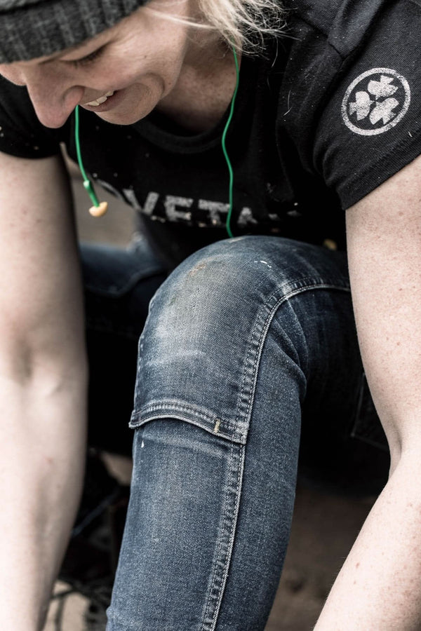 Woman wearing Dovetail Workwear Logo Tee in black, shown from above while looking down at her blue jeans, displaying the classic logo on the chest