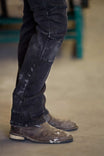 Detail view of a woman's legs wearing Dovetail Workwear's Britt Utility Pant in Black Stretch Thermal Denim with reinforced knees, paired with work boots