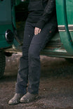 Woman wearing Dovetail Workwear Britt Utility Pant in Black Stretch Thermal Denim standing against a green truck, showing the straight leg fit and reinforced knee detail