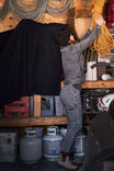 Woman reaching for yellow rope in a workshop wearing Dovetail Workwear Maven X Slim Pant in Grey Stretch Thermal Denim, showcasing the reinforced construction and slim fit
