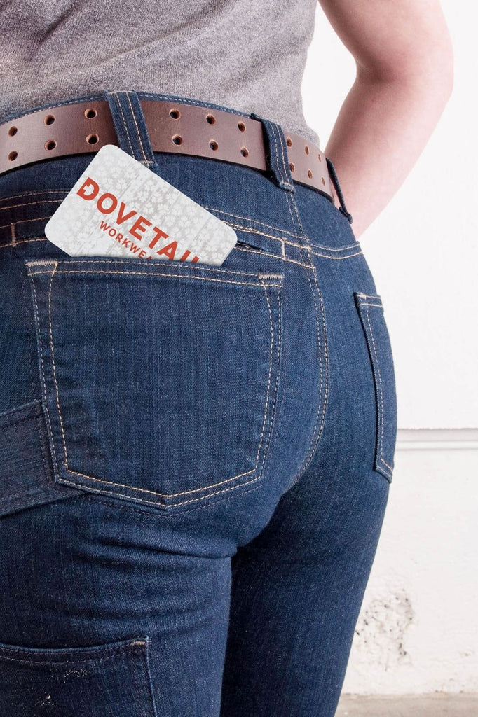 Dovetail Workwear Gift Certificate displayed in the back pocket of dark blue jeans worn by a woman, featuring the brand logo in red text on white card